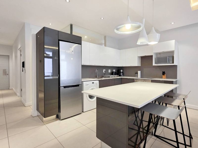 Modern kitchen featuring high-gloss cabinetry, a central island with breakfast bar seating, integrated appliances, and sleek tiled flooring.