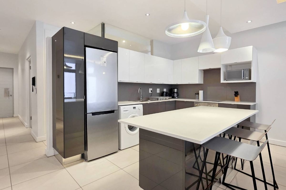 Modern kitchen featuring high-gloss cabinetry, a central island with breakfast bar seating, integrated appliances, and sleek tiled flooring.
