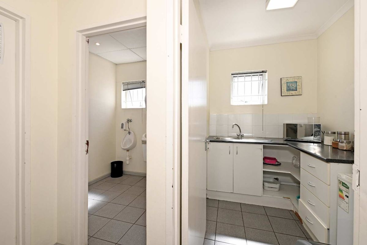 A functional industrial kitchenette featuring built-in cabinetry, a stainless steel sink, and an adjacent restroom facility with a wall-mounted urinal.