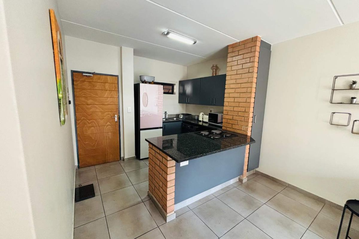 Compact kitchen featuring dark cabinetry, granite countertops, a built-in hob, and a distinctive brick-accented breakfast bar.