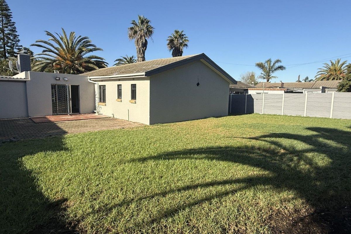 Rear view of the property featuring a paved patio area, a well-maintained lawn, and secure boundary walling.