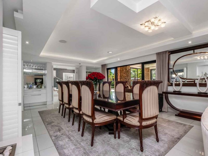Elegant dining room featuring a coffered ceiling, tiled flooring, and a built-in bar area, with seamless access to the outdoor patio through sliding glass doors.