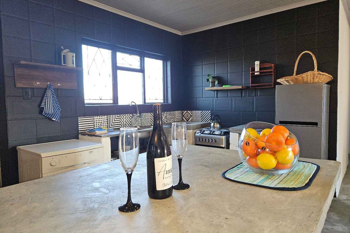 A rustic kitchen featuring dark painted block walls, a concrete island bench, and a built-in sink area with patterned tile splashbacks.