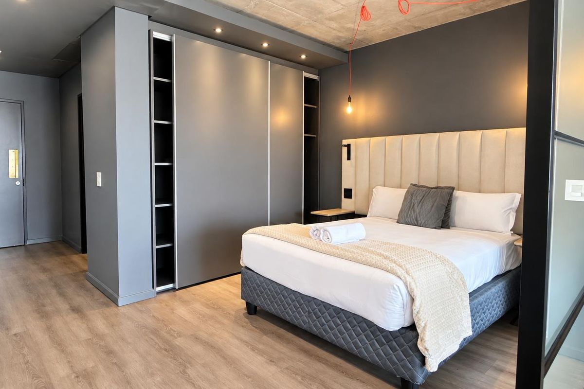 Modern bedroom featuring exposed concrete ceilings, laminate flooring, built-in wardrobes with integrated lighting, and a sleek glass partition.