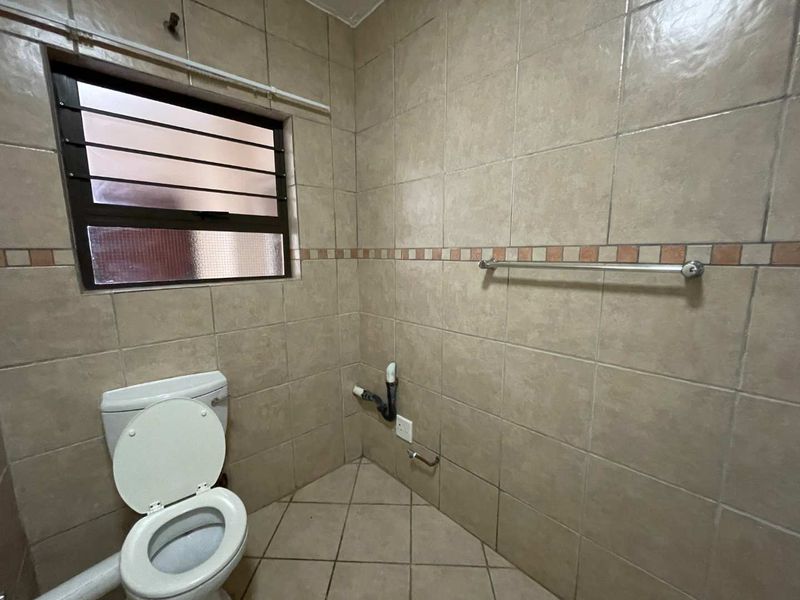 A small bathroom featuring tiled walls and flooring, equipped with a toilet and exposed plumbing, awaiting a vanity or basin installation.