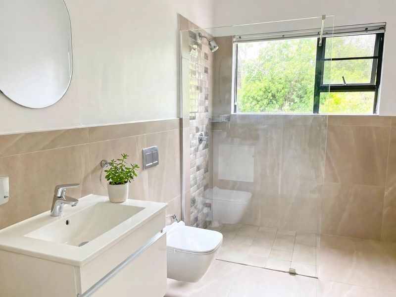 Modern bathroom featuring a wall-mounted vanity, wall-hung toilet, bidet, and a spacious walk-in shower with a glass screen and neutral tiling.