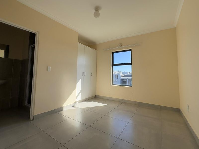 A bright, empty bedroom featuring neutral tiled flooring, built-in cupboards, and a window providing natural light.