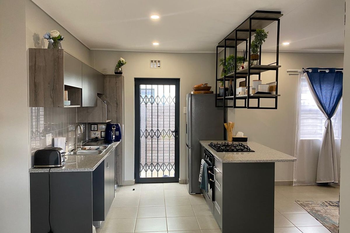 Modern kitchen featuring dark cabinetry, stone countertops, a central island with a built-in gas hob, and a security gate leading to the exterior.