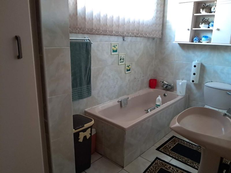 A functional bathroom featuring a built-in bathtub, pedestal basin, toilet, and tiled finishes, offering a classic layout with potential for modern updates.