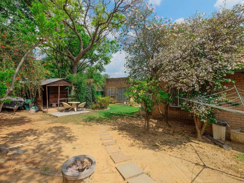 A spacious rear garden featuring a brick exterior, mature trees, a wooden shed, a concrete fire pit, and a rotary clothesline.