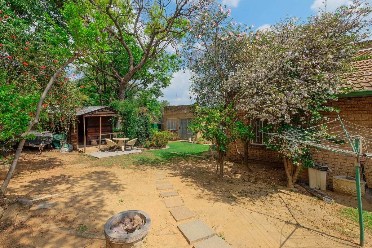 A spacious rear garden featuring a brick exterior, mature trees, a wooden shed, a concrete fire pit, and a rotary clothesline.