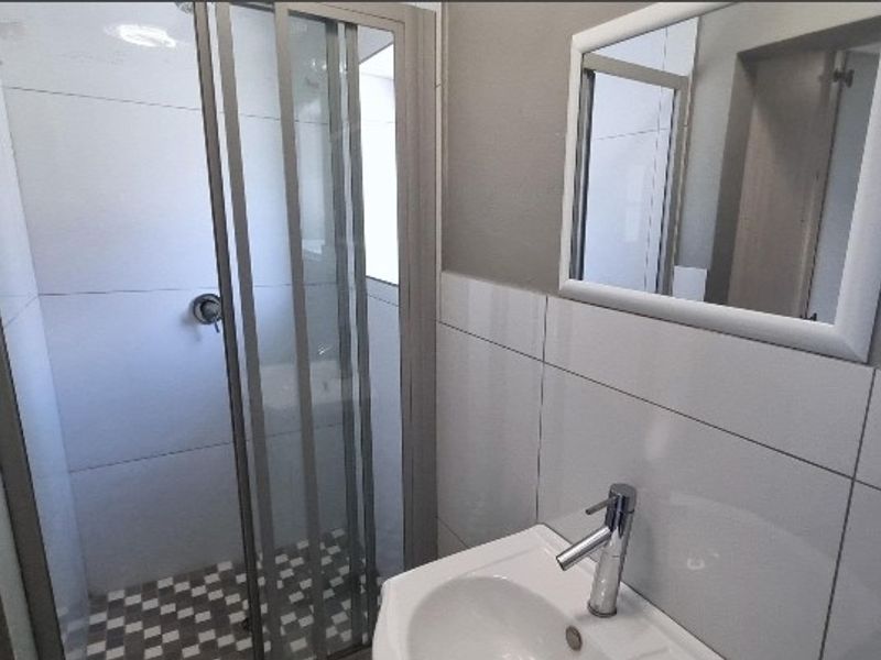 A clean, modern bathroom featuring a glass shower enclosure, white tiled walls, a vanity basin with a mixer tap, and a wall-mounted mirror.