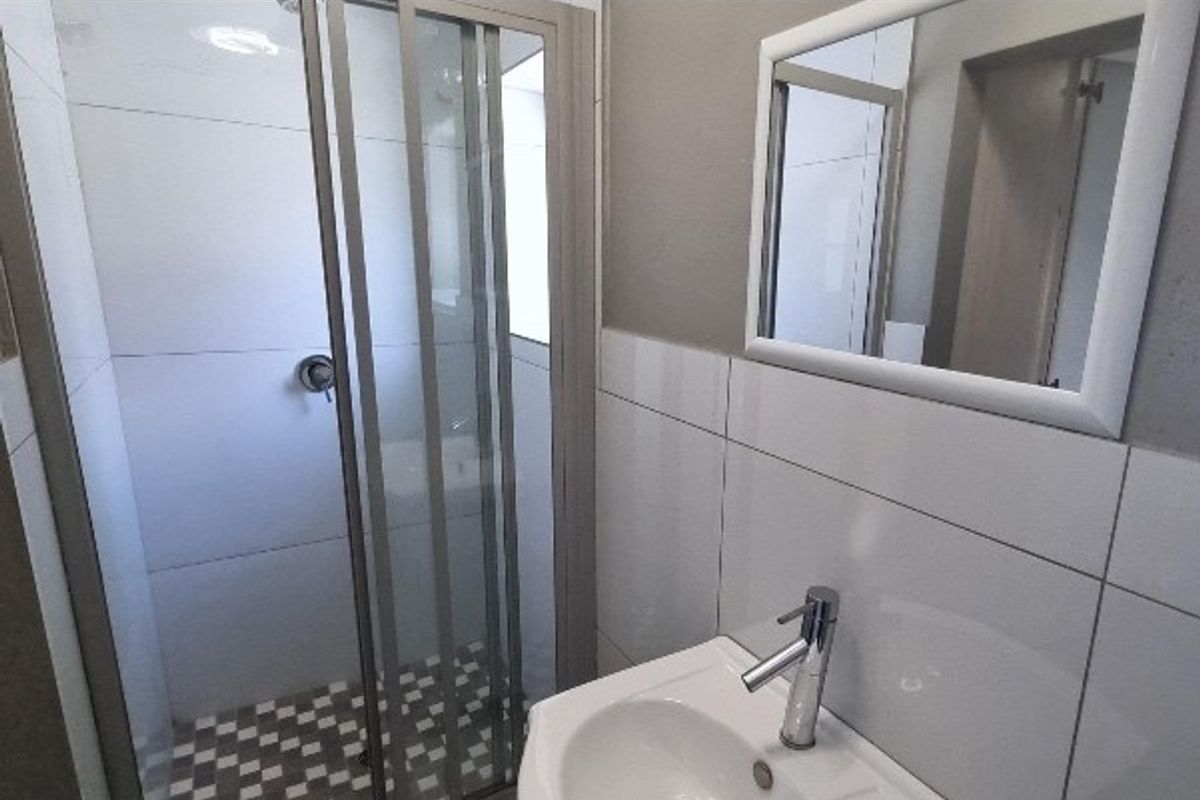 A clean, modern bathroom featuring a glass shower enclosure, white tiled walls, a vanity basin with a mixer tap, and a wall-mounted mirror.