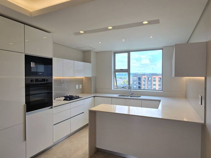 Modern kitchen featuring high-gloss cabinetry, integrated appliances, quartz countertops, and recessed lighting, offering a clean and contemporary aesthetic.
