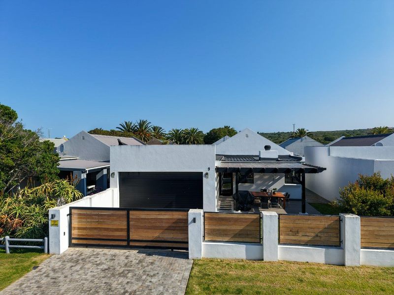 Front view of a modern house featuring a paved driveway, secure timber and steel fencing, an automated garage, and a covered outdoor patio area.