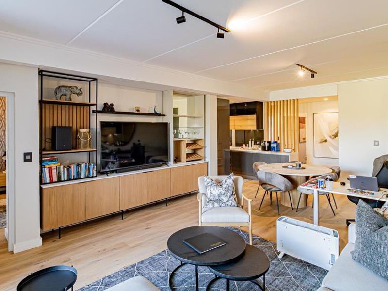 Spacious open-plan living area featuring timber flooring, modern track lighting, and custom built-in cabinetry, seamlessly connecting to the dining space and adjacent bedroom.