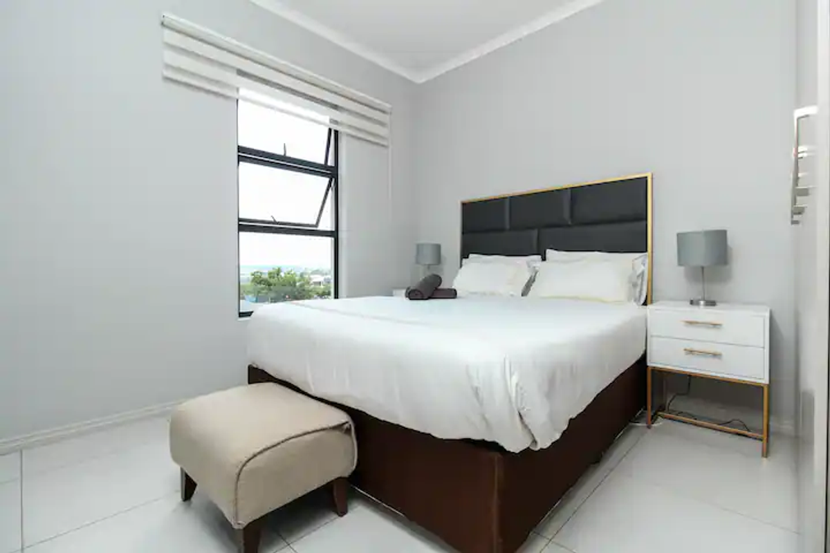 A bright and modern bedroom featuring tiled flooring, neutral walls, and a large window with fitted blinds.
