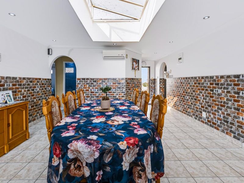 Spacious dining area featuring a large central skylight, brick veneer wall accents, tiled flooring, and arched architectural transitions to adjacent rooms.