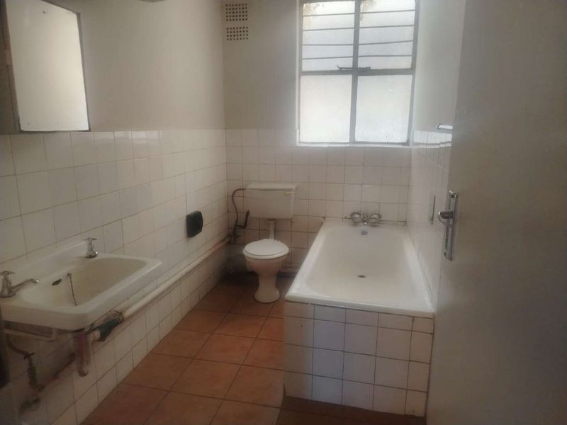 A dated, empty bathroom featuring tiled walls and floors, a standard bathtub, toilet, and pedestal basin, requiring modernization and cosmetic updates.