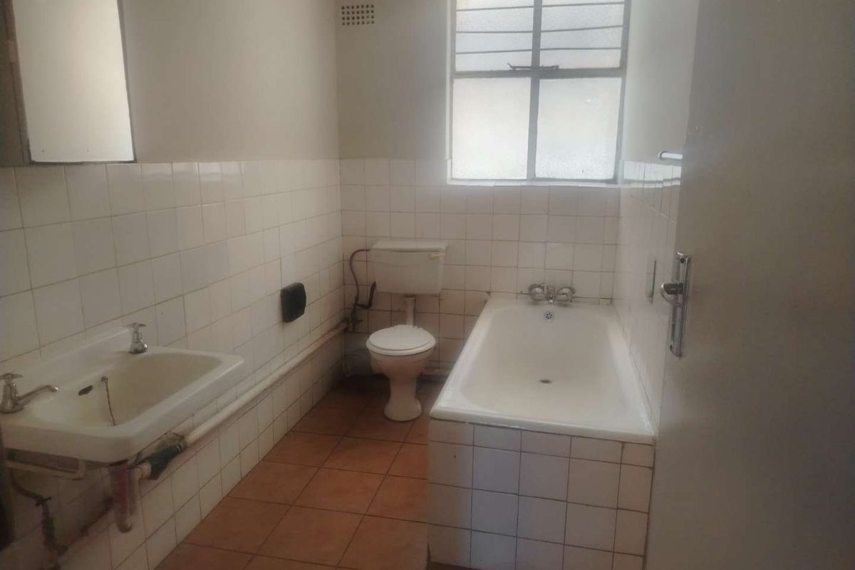 A dated, empty bathroom featuring tiled walls and floors, a standard bathtub, toilet, and pedestal basin, requiring modernization and cosmetic updates.