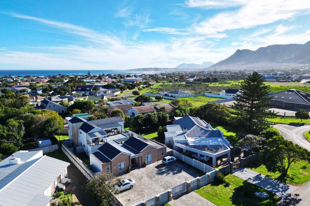Aerial view of the property showcasing the building layout, paved driveway, perimeter fencing, and surrounding coastal neighbourhood with mountain views.