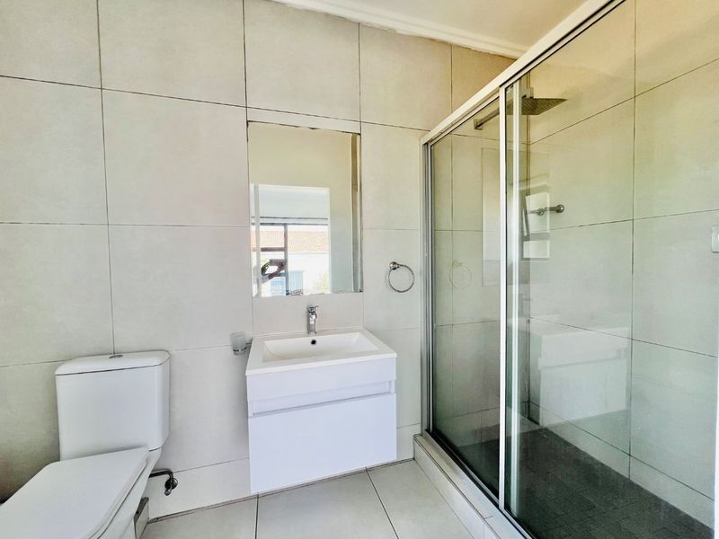 Modern bathroom featuring a wall-mounted vanity with basin, a glass-enclosed shower, and neutral floor-to-ceiling tiling.