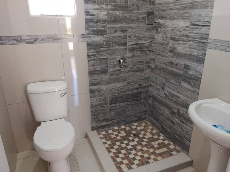 A clean, functional bathroom featuring a pedestal basin, a standard toilet, and a walk-in shower with decorative tiled flooring and wall finishes.