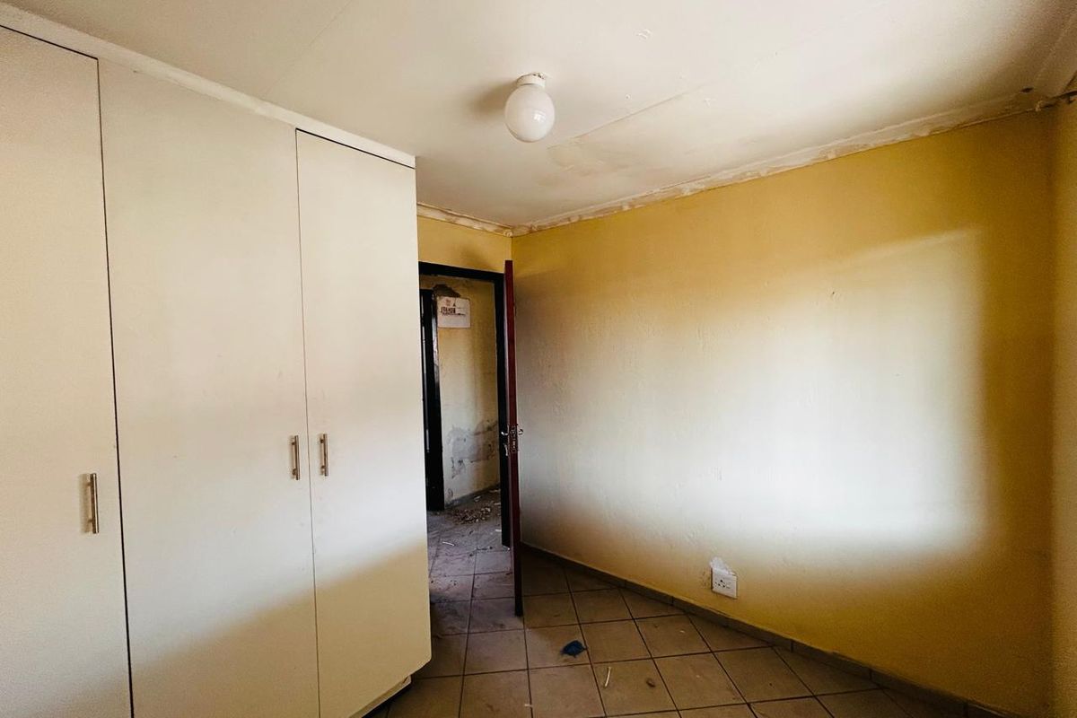 A vacant bedroom featuring built-in wardrobes and tiled flooring, requiring cosmetic updates and repairs to the walls and ceiling.