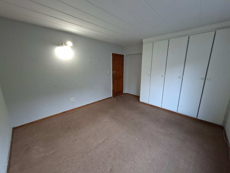 A vacant bedroom featuring built-in cupboards, carpeted flooring, and a timber door, offering a blank canvas for potential updates.