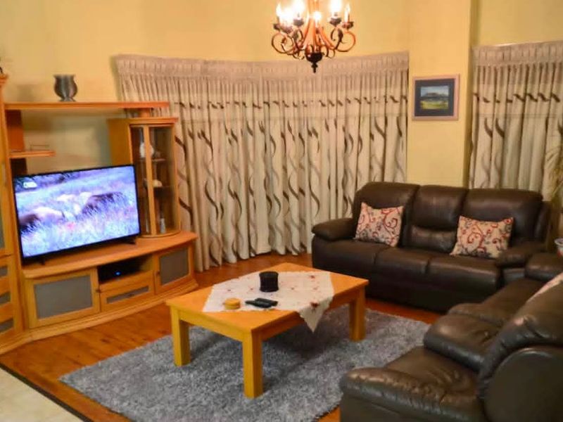 A comfortable living room featuring warm hardwood flooring and a central decorative chandelier, providing a cozy and traditional atmosphere.
