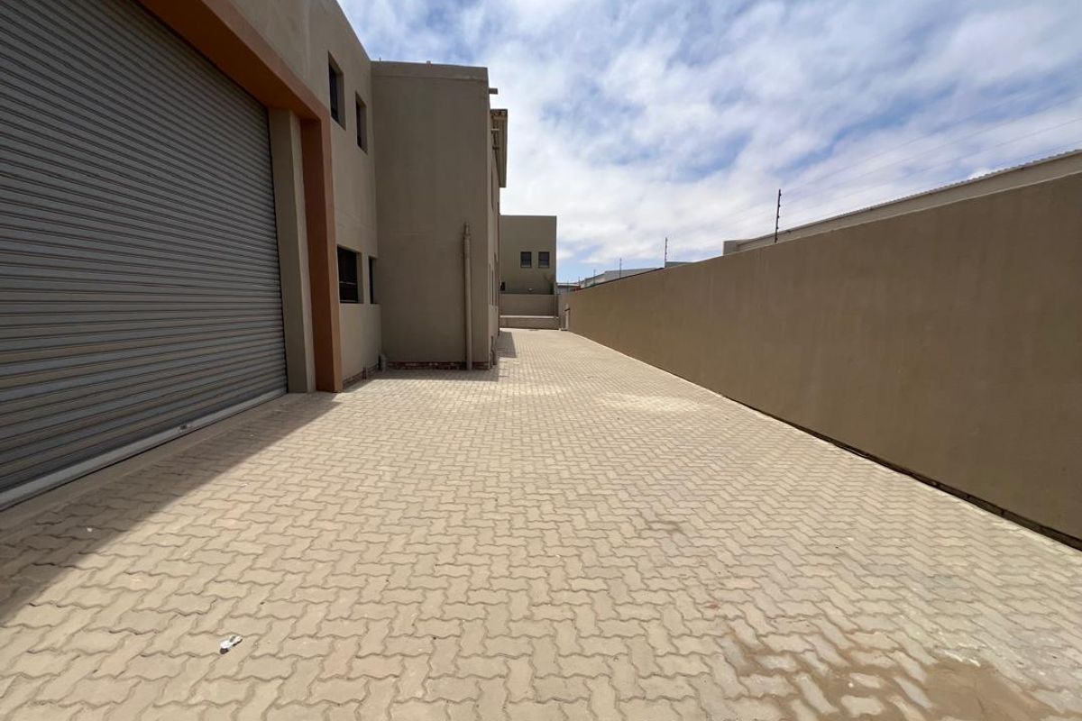 Spacious industrial exterior side yard featuring paved driveway access and a large roller shutter door for efficient loading and vehicle entry.