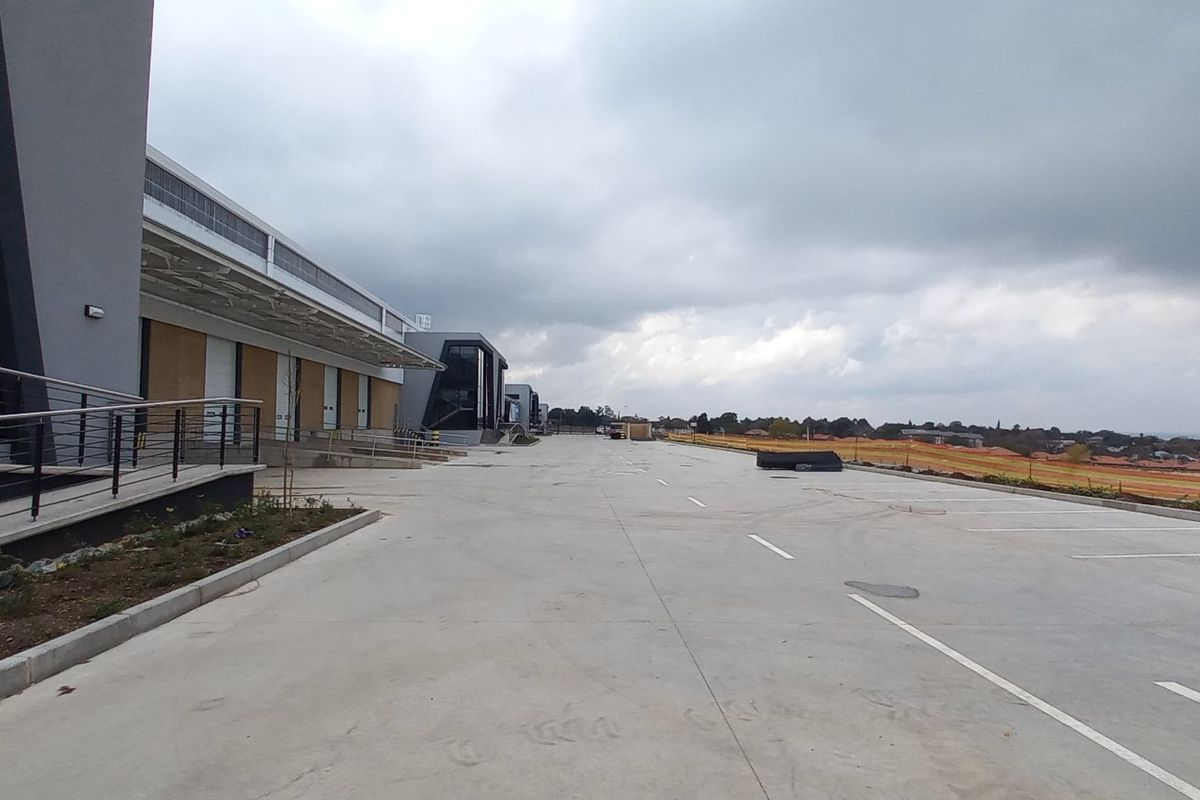 A modern industrial facility featuring a large concrete loading yard, professional facade with glass curtain walling, and integrated loading bays.