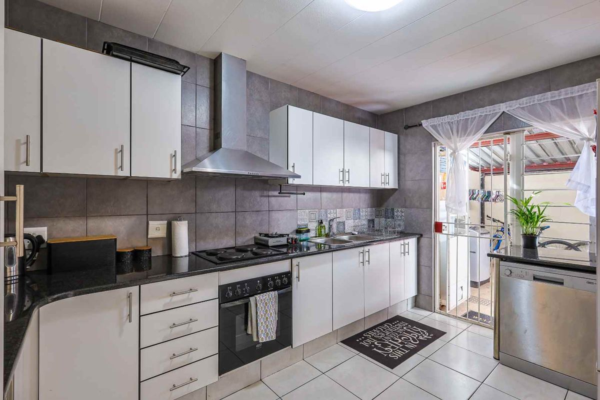 A functional kitchen featuring white cabinetry, dark granite countertops, a stainless steel extractor fan, built-in oven, and tiled flooring with direct access to the patio.
