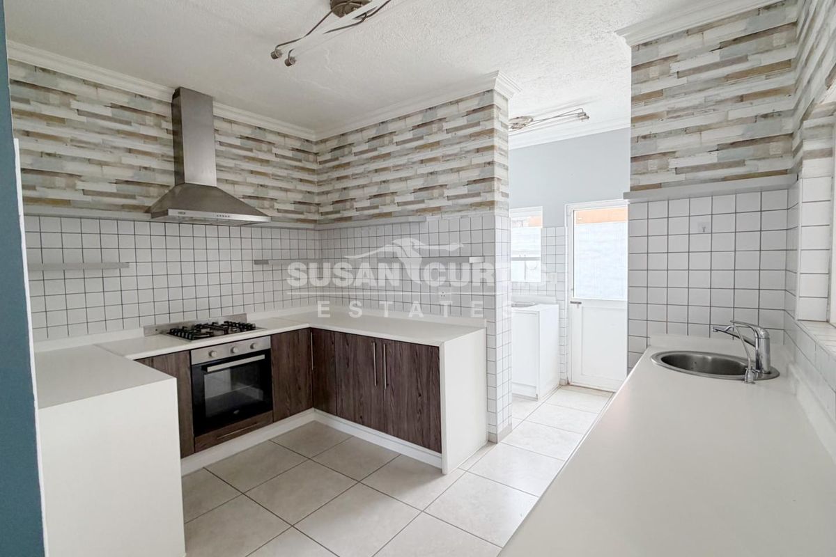 A clean, functional kitchen featuring built-in cabinetry, a gas hob with extractor fan, tiled splashbacks, and a separate scullery area with exterior access.