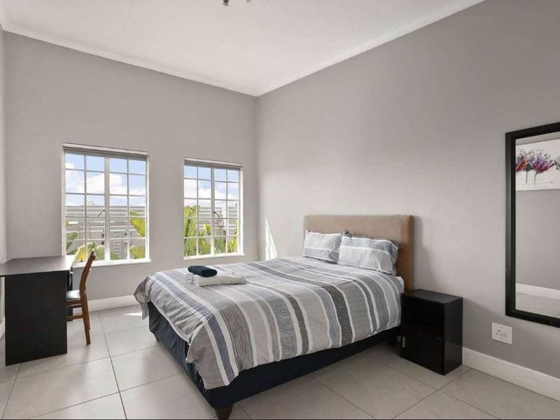 A well-lit bedroom featuring neutral grey walls, tiled flooring, and two windows providing natural light.