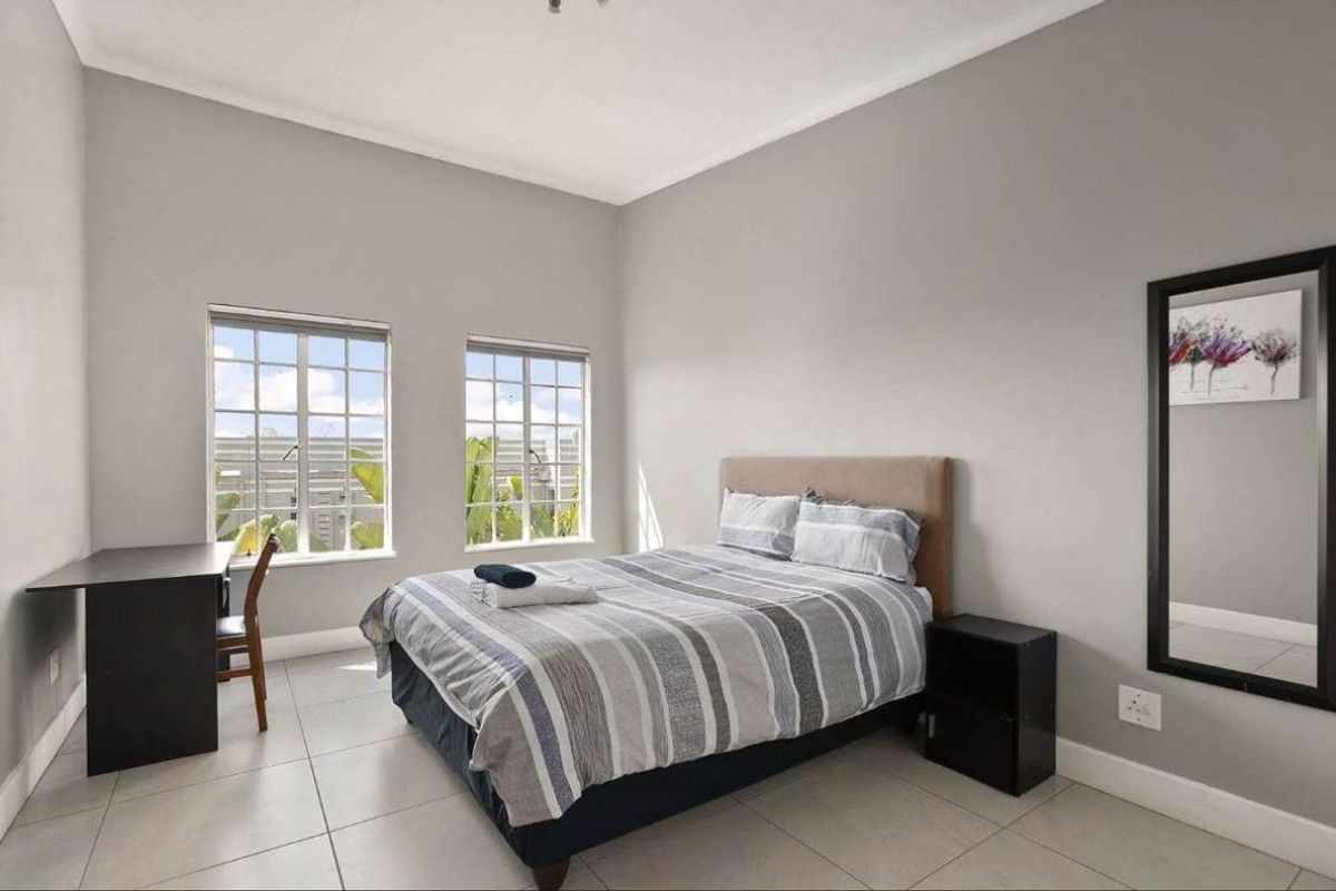 A well-lit bedroom featuring neutral grey walls, tiled flooring, and two windows providing natural light.