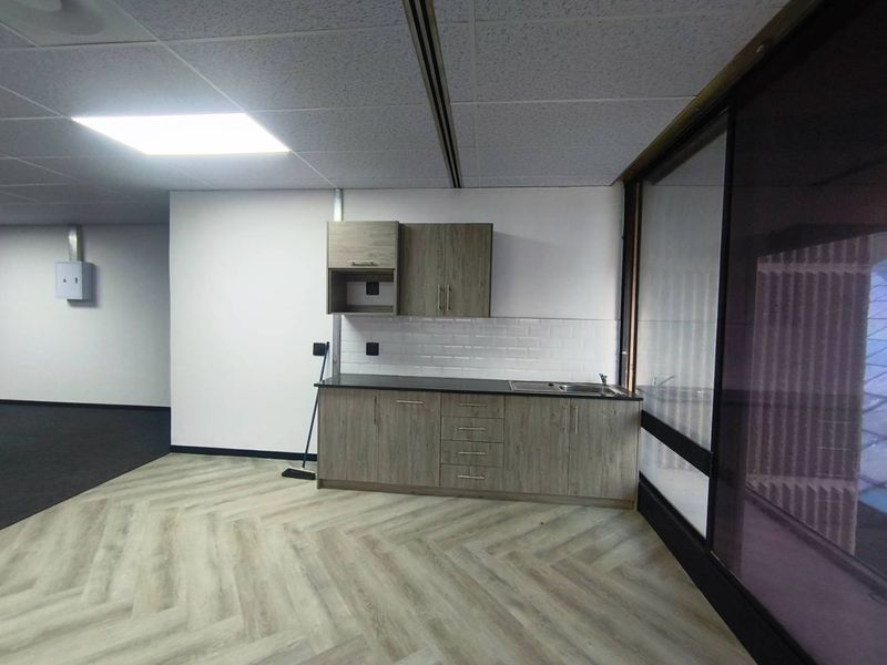 A modern office kitchenette featuring wood-grain cabinetry, a subway tile backsplash, stainless steel sink, and durable herringbone vinyl flooring.