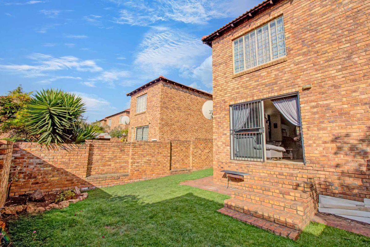 Rear view of a townhouse featuring a private garden, brick boundary walls, and a paved patio area with sliding door access.