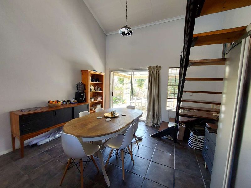 Open-plan living and dining area featuring vaulted ceilings, tiled flooring, and an open staircase leading to the upper level with access to the patio.