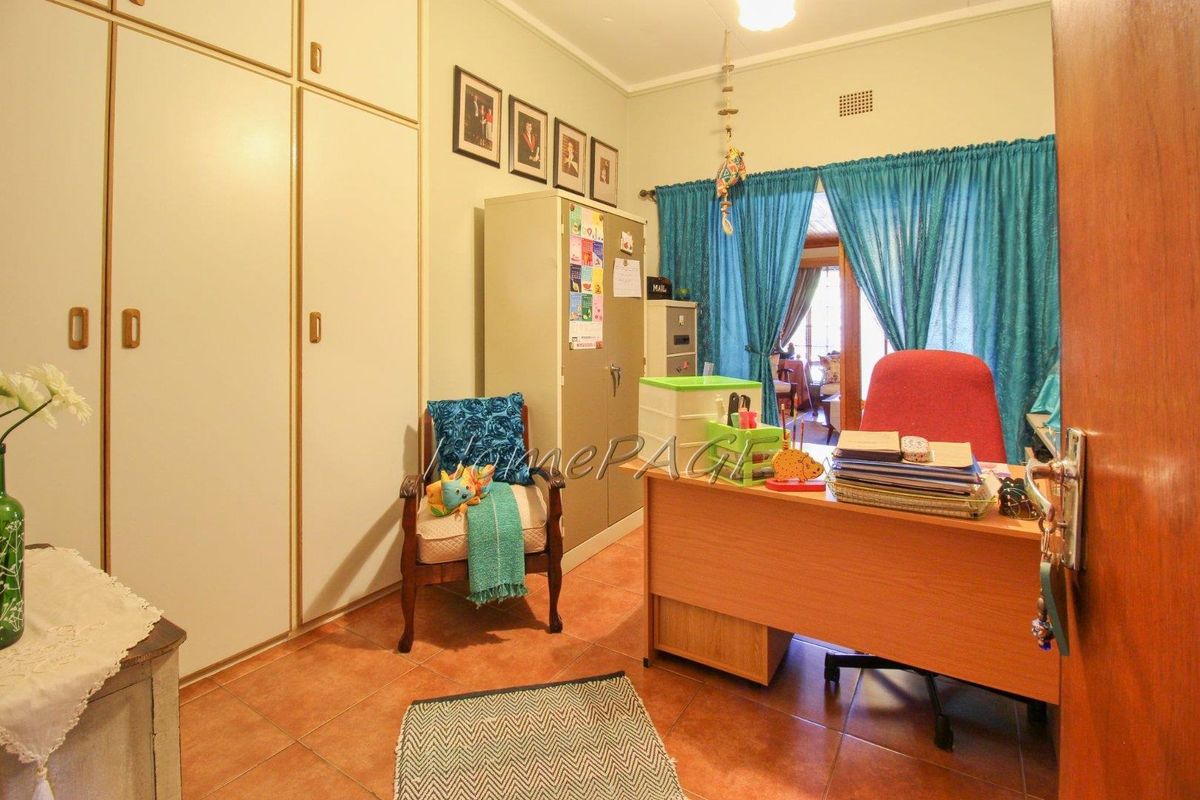A functional bedroom or home office featuring built-in floor-to-ceiling cupboards, tiled flooring, and access to an adjoining room through a curtained doorway.