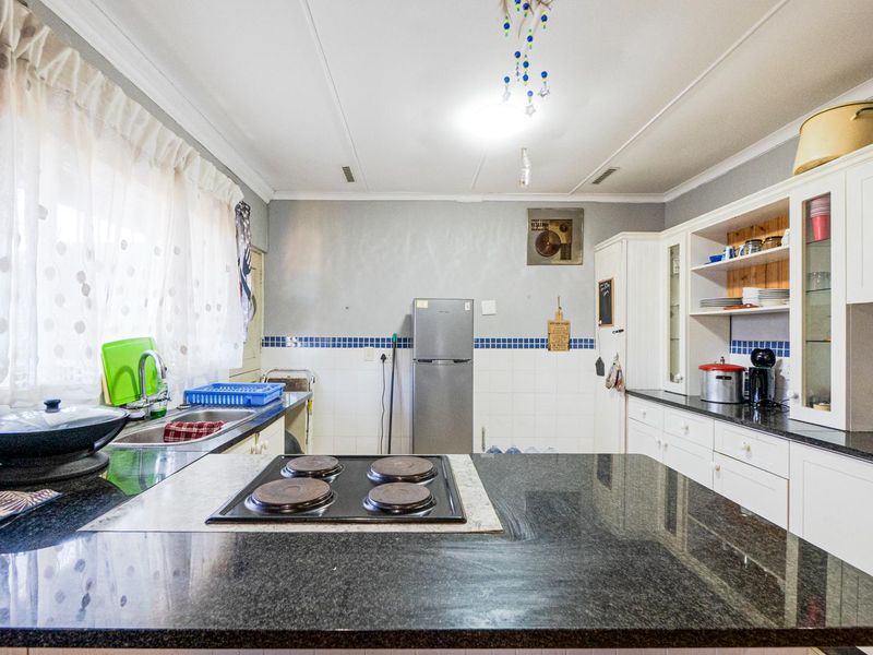 A functional kitchen featuring granite countertops, an integrated electric hob, ample built-in cabinetry, and a tiled backsplash.