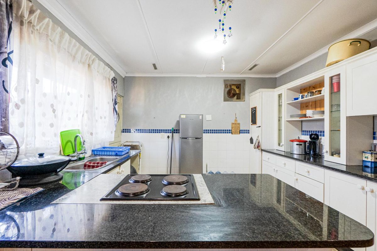 A functional kitchen featuring granite countertops, an integrated electric hob, ample built-in cabinetry, and a tiled backsplash.