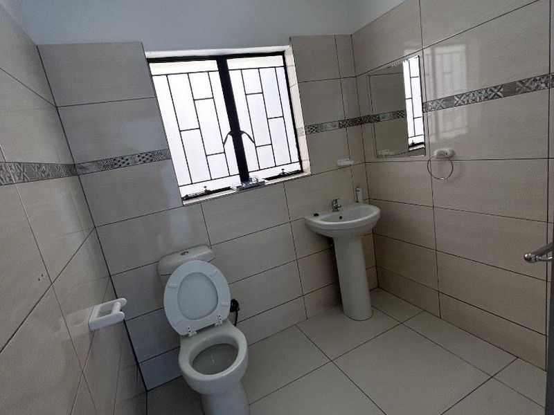 A clean, tiled bathroom featuring a pedestal washbasin, toilet, and a window with security bars.