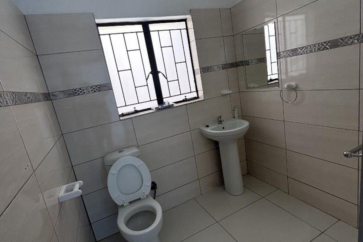 A clean, tiled bathroom featuring a pedestal washbasin, toilet, and a window with security bars.