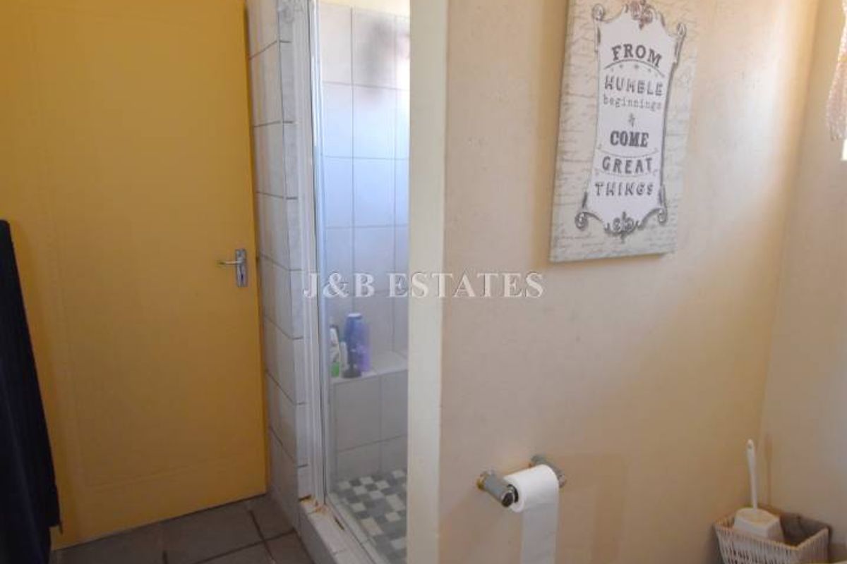 A functional bathroom featuring a tiled shower enclosure, a standard toilet, and tiled flooring.