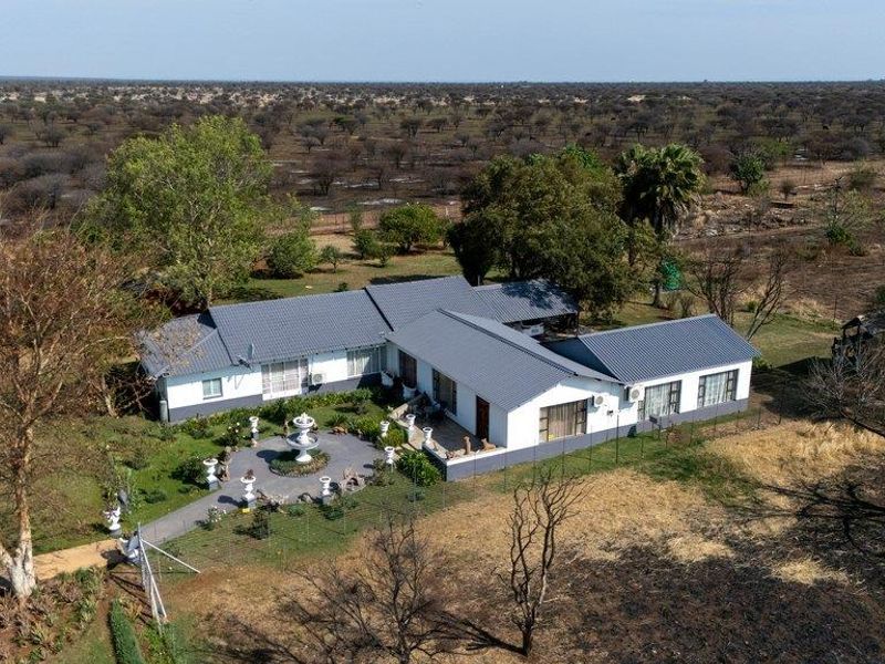 Aerial view of a farm property featuring a main dwelling with a metal roof, a paved courtyard with a fountain, and surrounding rural landscape.