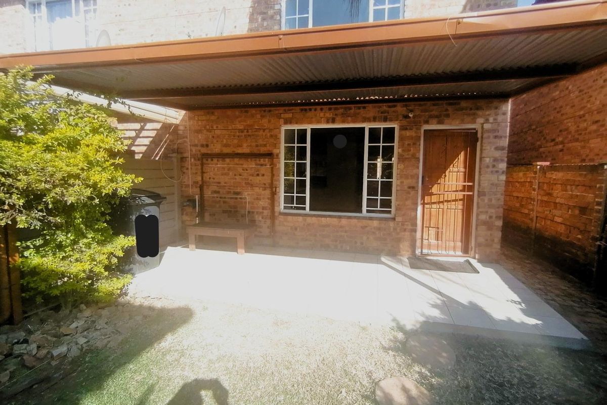 Rear exterior view of the townhouse featuring a covered patio area with a corrugated metal roof, brick facade, and secure entrance door.