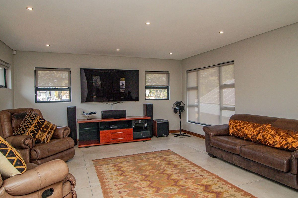 A comfortable living room featuring tiled flooring, recessed downlighting, and multiple windows with fitted roller blinds.