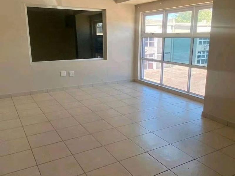A bright, empty living area featuring neutral tiled flooring, large aluminium windows, and an internal service window, offering a clean canvas for interior design.