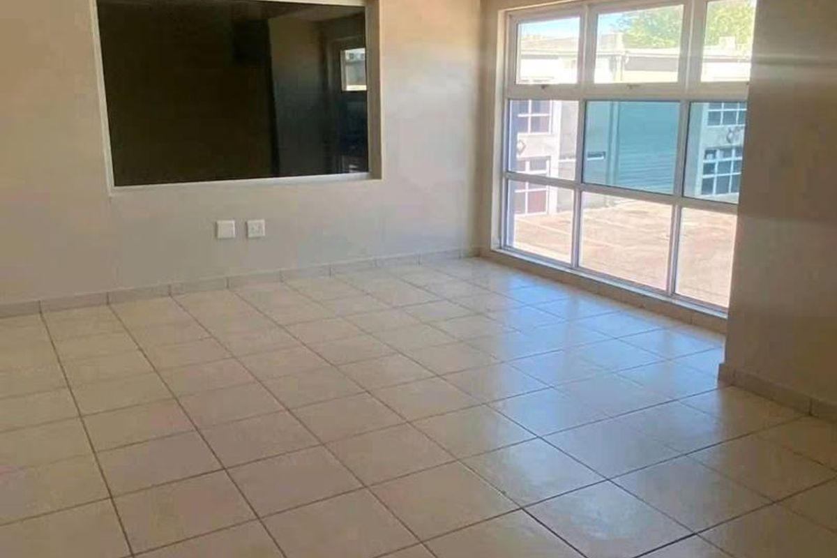 A bright, empty living area featuring neutral tiled flooring, large aluminium windows, and an internal service window, offering a clean canvas for interior design.